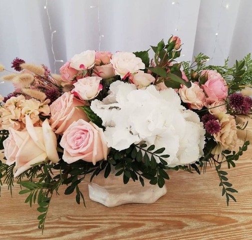 Un centro floral elegante con flores frescas y follaje verde, dispuesto sobre una mesa de madera rústica